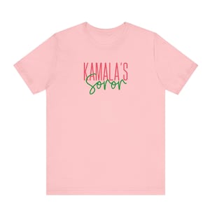 May include: Pink short-sleeved t-shirt with the text "KAMALA'S SOROR" in red and green.