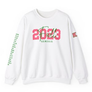 May include: White sweatshirt with a pink and green 'Fall 2023' graphic on the front and a green 'K' on the left sleeve. The text 'G.E.N.E.S.I.S.' is printed below the graphic.