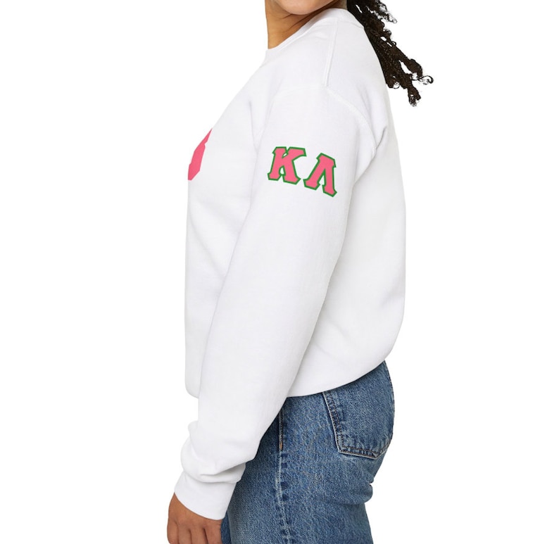 May include: White sweatshirt with a pink and green Greek letter design on the sleeve. The letters are "KA".