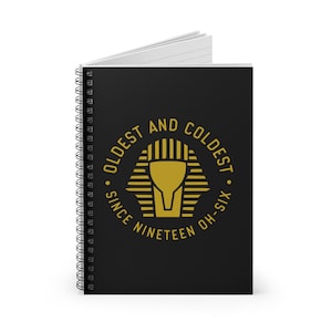 May include: Black spiral notebook with a gold graphic of an Egyptian pharaoh's head with the text "Oldest and Coldest. Since Nineteen Oh-Six."