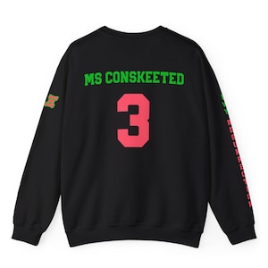 May include: Black sweatshirt with green and pink text on the back. The text reads "MS CONSKEETED" and "3". The sleeves have green and pink text that reads "MY RESURRECTION".