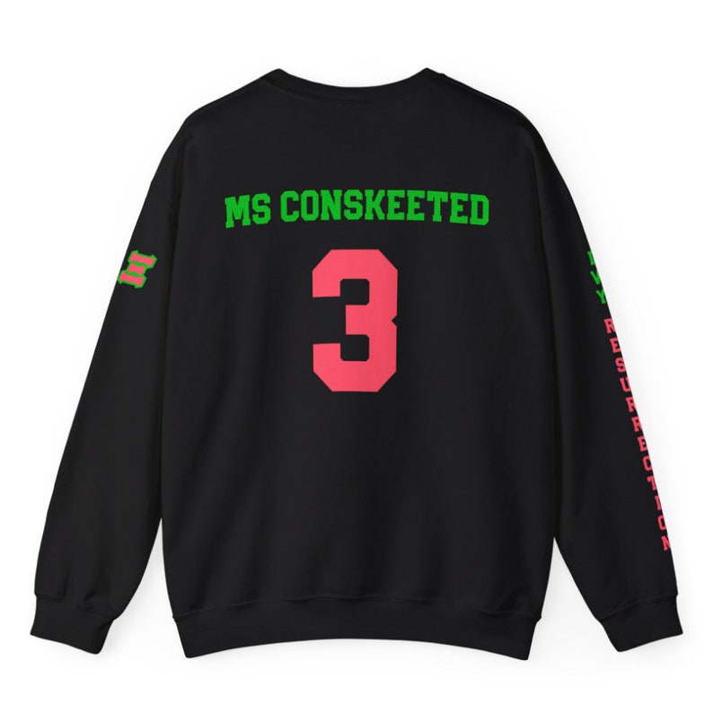 May include: Black sweatshirt with green and pink text on the back. The text reads "MS CONSKEETED" and "3". The sleeves have green and pink text that reads "MY RESURRECTION".