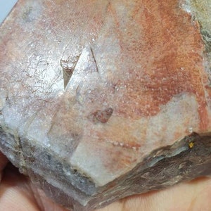 May include: A large, clear quartz crystal with a reddish-brown hue. The crystal has a natural, rough surface and is shaped like a pyramid.