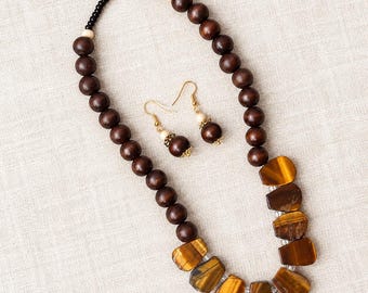 May include: A jewellery set consisting of a necklace and matching earrings. The necklace features dark brown wooden beads, cream-coloured accents, and a series of polished tiger eye stone pendants. The earrings feature matching beads and stones.