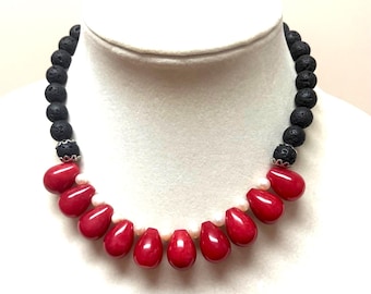May include: A necklace featuring a strand of round black porous lava beads and a series of smooth, teardrop-shaped red beads. Small white pearls are interspersed between the red teardrop beads, and silver-toned metal spacers accent the lava beads.