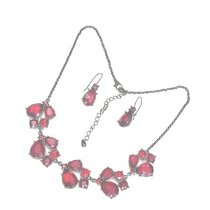 Pu&ograve; includere: Un set di collana e orecchini color canna di fucile scuro. La collana presenta una serie di pietre rosse a forma di goccia raggruppate. Gli orecchini abbinati hanno una singola pietra rossa a forma di goccia.