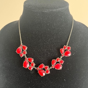 Pu&ograve; includere: Una collana appariscente con gruppi di pietre rosse a forma di goccia. Le pietre sono incastonate in un metallo dorato, creando un design audace. La collana &egrave; esposta su un manichino nero.