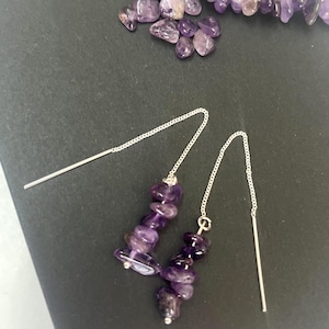 May include: A pair of silver-tone threader earrings featuring dangling clusters of polished, irregular purple amethyst chip beads. The earrings consist of a thin metal chain with a straight post at one end and the amethyst stones at the other.