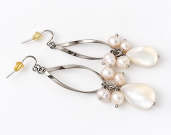 May include: A pair of drop earrings featuring a twisted silver-tone metal teardrop frame. Each earring is adorned with a cluster of small, round, off-white freshwater pearls and a single, larger, smooth, pear-shaped white shell pendant.