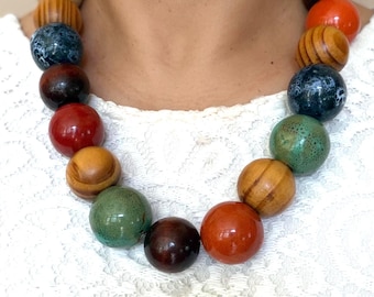 May include: A statement necklace featuring a series of large, spherical beads in a variety of finishes. The beads include polished solid colours in red, dark brown, and orange, natural wood grain textures, and mottled blue and green speckled patterns.