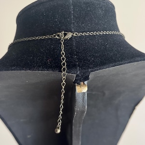 Pu&ograve; includere: Primo piano del retro di una collana su un espositore nero. La collana ha una catena delicata e una catena di estensione regolabile con una piccola sfera all'estremit&agrave;. Il metallo ha una finitura scura e antica.