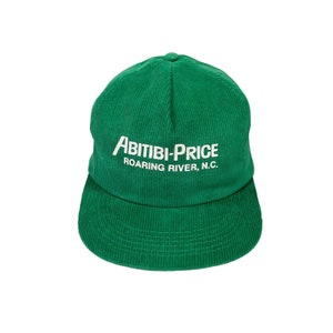 May include: A green corduroy baseball cap with the text "Abitibi-Price Roaring River, N.C." embroidered in white on the front.