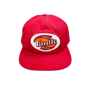 May include: Red baseball cap with a white oval patch featuring the text "Tindle" in a red and orange font with the years "1896" and "1996" above and below the text.