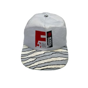 Può includere: Un berretto da baseball blu chiaro con visiera a righe bianche e nere. La parte anteriore del berretto presenta un logo rosso e nero che dice "Matco Tools Series 5".