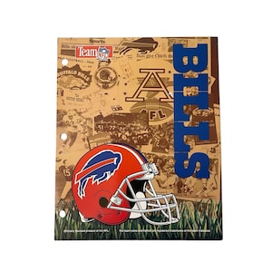 May include: A Buffalo Bills themed notebook with a collage background of newspaper clippings and football imagery. The notebook features a red and blue helmet graphic and the word "BILLS" in blue block letters.