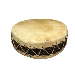Può includere: Un tamburo rotondo con una pelle di colore marrone chiaro e un corpo intrecciato marrone scuro. La pelle è tesa sul corpo e fissata con un cordoncino marrone chiaro. È uno strumento musicale.