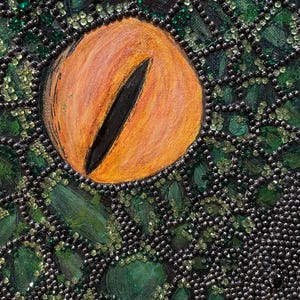 May include: A detailed painting of a reptilian eye with a bright orange iris and a vertical black pupil. The surrounding skin is textured with shades of dark green and black, embellished with numerous small, reflective beads and crystals.