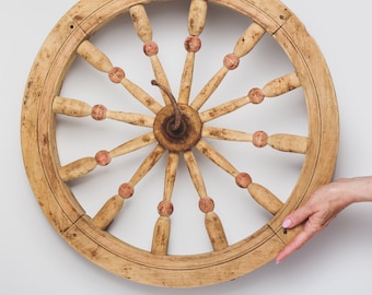 May include: A wooden spinning wheel with a circular frame and spokes with pink accents. The wheel is made of light brown wood and has a rustic appearance.