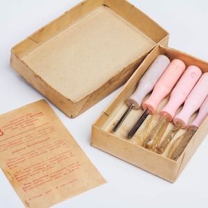 Może przedstawiać: Zestaw pięciu narzędzi do rzeźbienia w drewnie z różowymi i fioletowymi uchwytami w kartonowym pudełku. Narzędzia są oznaczone "СОВЕТСКАЯ ПРОМЫШЛЕННОСТЬ" i "СССР".