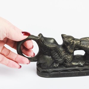May include: A bronze winged griffin sculpture with a round, flat top. The griffin is holding the top in its mouth and has a ring on its back.