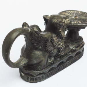 May include: A black metal incense burner shaped like a mythical creature with a round, flat top. The creature has a ring handle and sits on a base with a decorative pattern.