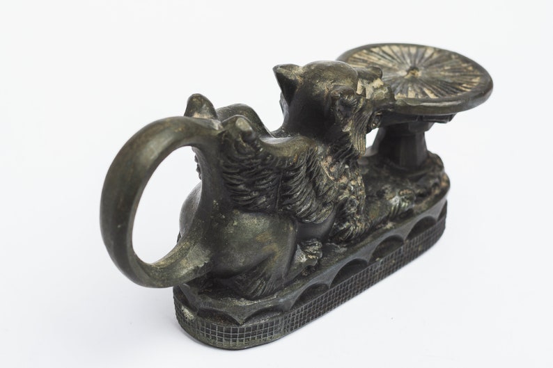 May include: A black metal incense burner shaped like a mythical creature with a round, flat top. The creature has a ring handle and sits on a base with a decorative pattern.