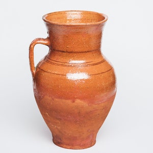 May include: A brown ceramic pitcher with a wide mouth and a handle. The pitcher has a rustic, handmade look.