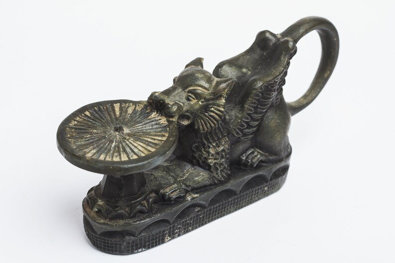 May include: A black metal incense burner shaped like a mythical creature with wings and a round dish on top. The creature is holding the dish in its mouth.