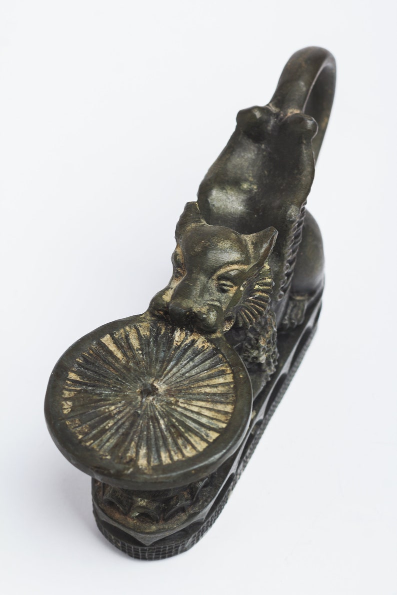 May include: A dark bronze incense burner shaped like a mythical creature with a round, decorative top. The creature is holding its head up and has a ring on its back.