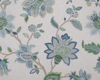 May include: A white fabric featuring an intricate embroidered floral pattern in shades of light blue, dark blue, and green. The design consists of large, multi-petaled blossoms and smaller buds connected by thin, light brown embroidered stems.