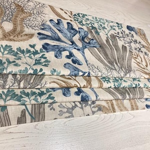 May include: A beige roman shade with a blue and brown sea life pattern. The shade is folded and has a textured fabric.