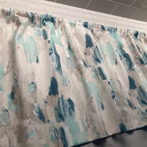 May include: A white valance with a teal and aqua abstract brushstroke pattern. The valance is made of a textured fabric and has a gathered look.