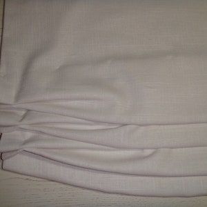 May include: White fabric roman shade with pleats. The shade is made of a textured linen-like material.