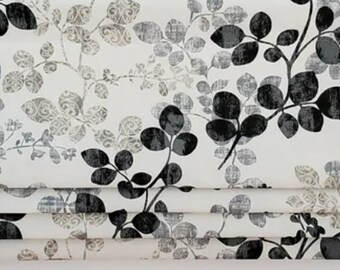 May include: White roman shade with a black and gray leaf pattern. The shade is made of a soft, textured fabric.