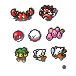 Può includere: Un set di nove personaggi Pokémon in pixel art, tra cui Krabby, Jigglypuff e Clefairy, realizzati con perline colorate.
