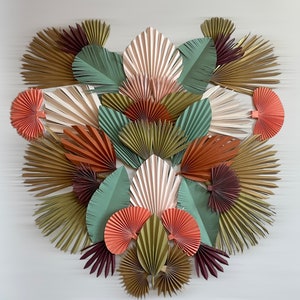 May include: A collection of paper fans in various colors and patterns, including green, brown, pink, and orange. The fans are arranged in a circular pattern, creating a decorative wall art piece.