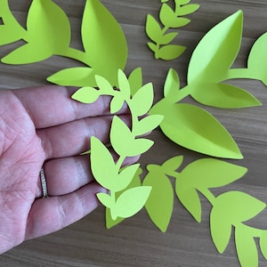 Puede incluir: Un conjunto de cinco hojas de papel verde, cortadas en forma de ramas con múltiples hojas. Las hojas están dispuestas sobre una superficie de madera.