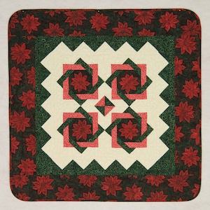 May include: A red and green quilted throw featuring a geometric design with a white background. The border is a red and green floral pattern.