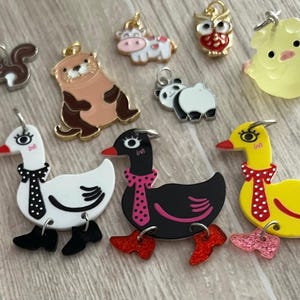 May include: A collection of colorful animal-themed charms, including a squirrel, otter, owl, duck, goose, and panda. The charms are made of metal and enamel, with gold-tone accents. The charms are designed for jewelry making or crafting.
