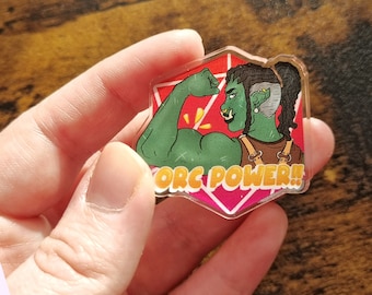 Può includere: Un orco verde con dreadlocks flette il bicipite su uno sfondo rosa e bianco. Il testo "ORC POWER!" è scritto in lettere gialle.