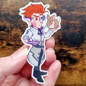 Pu&ograve; includere: Un adesivo in vinile fustellato raffigurante un personaggio dei cartoni animati con capelli arancioni a punta, che indossa un camice bianco sopra abiti scuri e un braccio meccanico viola. Il personaggio tiene in mano un piccolo coniglio marrone e indossa cuffie blu e rosse.