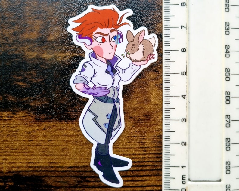 Pu&ograve; includere: Un adesivo fustellato raffigurante un personaggio con capelli arancioni, che indossa un camice bianco e guanti viola, mentre tiene in mano un piccolo coniglio marrone. Un righello accanto mostra un'altezza di circa 19 cm.