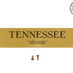 May include: Gold-colored metal plaque with the text "TENNESSEE" and "NESSIE" in black lettering. Two gold-colored screws are included.