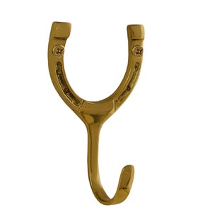 May include: A gold-colored horseshoe hook with a decorative design. The hook is attached to a wall with two screws.