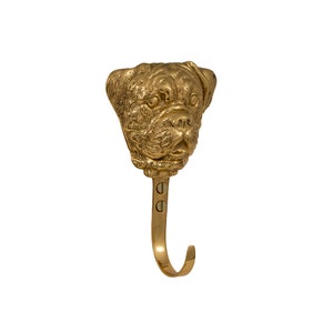 May include: A gold-toned brass hook with a bulldog head design. The hook is attached to a wall with two screws.