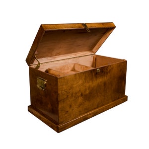 May include: A wooden storage chest with a hinged lid, brass hardware, and a divided interior. The chest is made of a light brown wood with a natural finish.