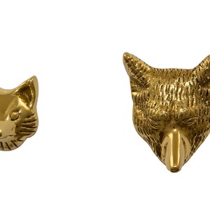May include: Two gold-colored fox head door knockers. The fox on the left has a more detailed face, while the fox on the right has a more stylized face.
