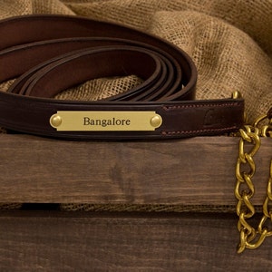 May include: A brown leather dog leash with a brass nameplate that reads "Bangalore" and a brass chain with a snap hook.