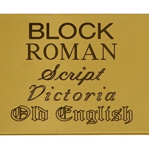 May include: A gold-coloured metal plaque with the words "BLOCK ROMAN", "Script", "Victoria", and "Old English" engraved in different fonts.