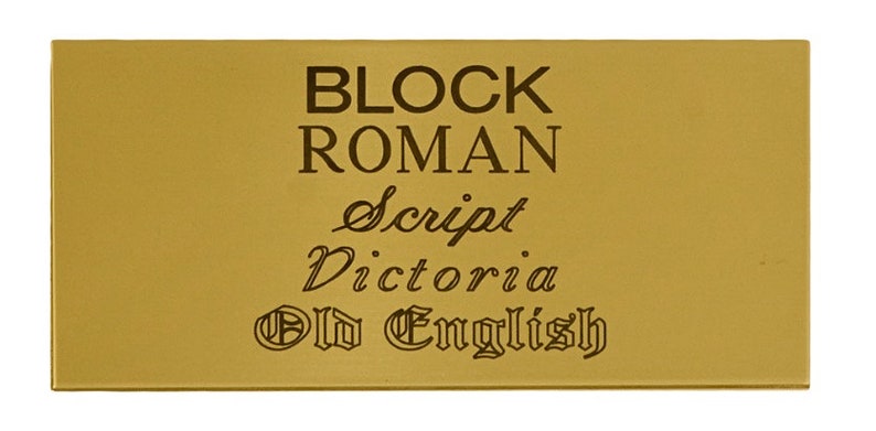 May include: A gold-coloured metal plaque with the words "BLOCK ROMAN", "Script", "Victoria", and "Old English" engraved in different fonts.